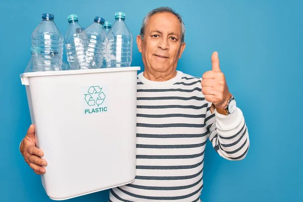 プラスチックボトルでゴミ箱を保持リサイクルシニア男は大きな笑顔で幸せな青色の背景をリサイクルすることができますOkサインをする 指で親指を立てる 優れたサイン — ストック写真