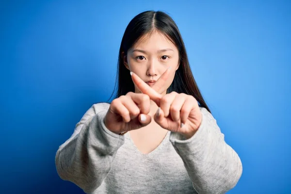 年轻美丽的亚洲女人穿着休闲装 站在蓝色孤立的背景上 用手指交叉表示拒绝 做阴性手势 — 图库照片