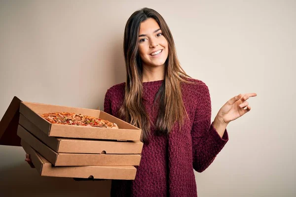 年轻而漂亮的姑娘拿着装有意大利披萨的送货盒 站在白色的背景上 非常高兴地手指手画脚地指向旁边 — 图库照片
