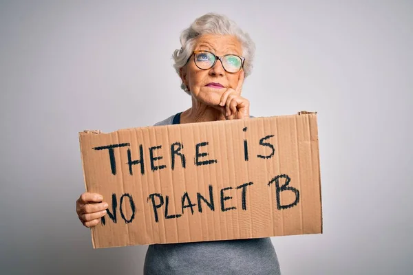Senior beautiful grey-haired woman asking for environment holding banner with earth message serious face thinking about question, very confused idea