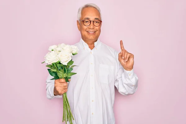 中年シニア白髪男保持ロマンチックな花束の白いバラ上ピンクの背景驚きでアイデアや質問を指差す指で幸せな顔 ナンバーワン — ストック写真