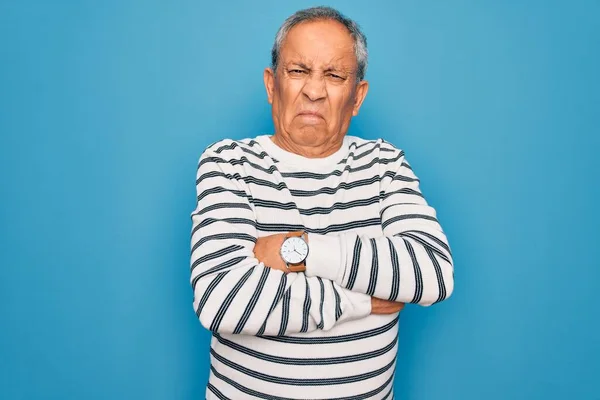 Senior handsome grey-haired man wearing striped sweater over isolated blue background skeptic and nervous, disapproving expression on face with crossed arms. Negative person.