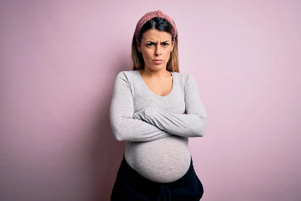 Young beautiful brunette woman pregnant expecting baby over isolated pink background skeptic and nervous, disapproving expression on face with crossed arms. Negative person.