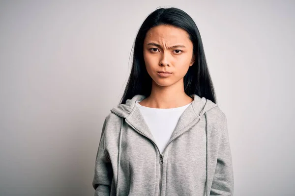 Young beautiful chinese sporty woman wearing sweatshirt over isolated white background skeptic and nervous, frowning upset because of problem. Negative person.