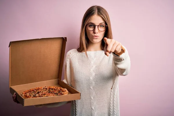 美しい赤頭の女性は カメラとあなたに指で指してピンクの背景にイタリアの新鮮なピザと宅配ボックスを保持します 手のサイン 正とフロントから自信を持ってジェスチャー — ストック写真
