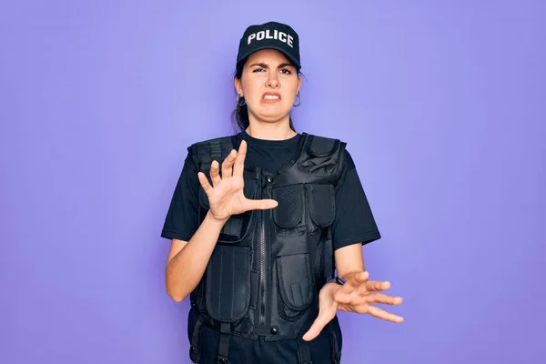 Young police woman wearing security bulletproof vest uniform over purple background disgusted expression, displeased and fearful doing disgust face because aversion reaction.
