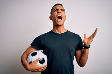 Yakışıklı Afro-Amerikan adam futbol topunu beyaz arka planda tutarak oynuyor deli gibi bağırıyor ve agresif bir ifade ve kollarla bağırıyor. Hayal kırıklığı konsepti.