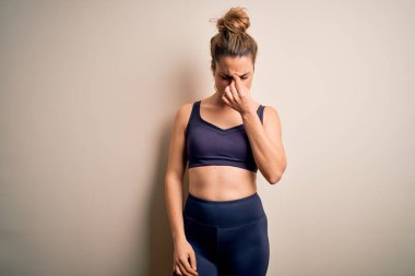 Genç ve güzel sarışın sporcu kadın spor giyer beyaz arka plan üzerine spor giyer burnu ve gözleri ovuşturur yorgunluk ve baş ağrısı hisseder. Stres ve hüsran kavramı.