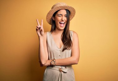 Genç ve güzel esmer kadın tatilde. Günlük elbiseler ve şapkalar giyip kameraya gülümsüyor. Zafer işareti yapıyor. İki numara..