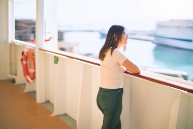 Tatilde mutlu ve kendinden emin gülümseyen genç ve güzel bir kadın. Yüzünde gülümsemeyle bir gemi güvertesinde durmak.