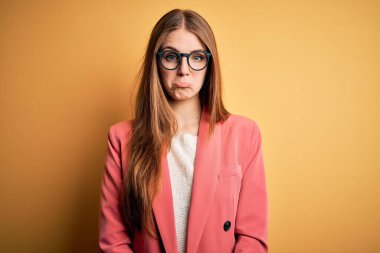 Ceket ve gözlük takan genç, güzel, kızıl saçlı bir kadın izole edilmiş sarı arka planda depresif ve üzüntülü, sinirli ve korkmuş bir şekilde ağlıyor. Üzücü ifade.