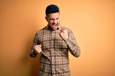 İzole edilmiş sarı arka plan üzerinde dikilmiş, kolları havada ve gözleri kapalı bir şekilde başarıyı kutlayan genç ve yakışıklı bir adam. Kazanan konsept.