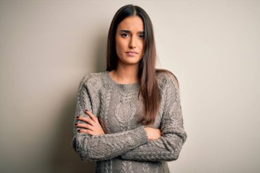Genç, güzel, esmer bir kadın izole edilmiş beyaz arka plan kuşkucu ve gergin, yüzünde çapraz kollu tasvip etmeyen bir ifade var. Negatif kişi.