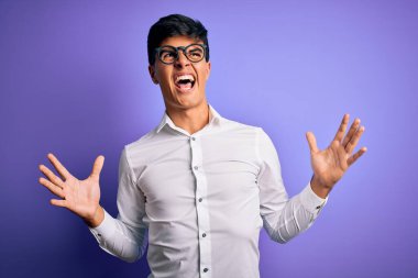 Mor arka plan üzerinde gömlek ve gözlük takan genç yakışıklı iş adamı sinirli bir ifadeyle bağırıyor ve kollarını kaldırıyor. Hayal kırıklığı konsepti.