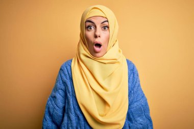 Genç, güzel, esmer, Müslüman kadın izole edilmiş sarı arka plan üzerine Arap başörtüsü takıyor. Şaşırmış ve şaşırmış bir ifade, korku ve heyecan dolu bir yüz..