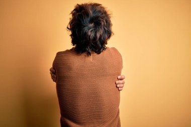 Sarı arka planda rahat gömleği ve süveteri olan genç yakışıklı bir adam mutlu ve pozitif bir şekilde sarılıyor. Sevgi ve özgüven.