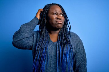Mavi arka planda örgü ören Afro-Amerikan kadın. Kafasını karıştırıyor ve soru soruyor. Şüpheyle kararsız, kafa kafaya düşünerek. Düşünceli kavram.