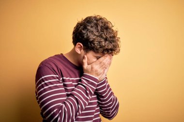 Sarışın, kıvırcık saçlı, sıradan çizgili süveter giyen, suratını ellerle kapatıp ağlayan genç, yakışıklı bir adam. Depresyon kavramı.