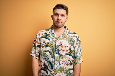 Tatilde mavi gözlü genç adam sarı arka planda çiçekli bir tişört giyiyor ve üzgün, sinirli ve korkmuş bir şekilde ağlıyor. Üzücü ifade.