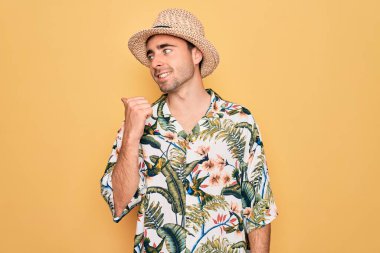 Tatilde mavi gözlü genç adam. Çiçek gömleği ve şapkası ile gülümsüyor. Gülümsüyor ve başparmağıyla yana bakıyor..