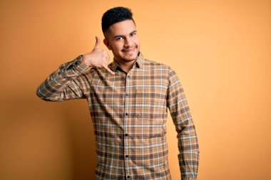 Izole sarı arka plan üzerinde duran rahat gömlek giyen genç yakışıklı adam telefonda konuşurken gibi el ve parmakları ile telefon jest yapıyor gülümseyerek. İletişim kavramları.