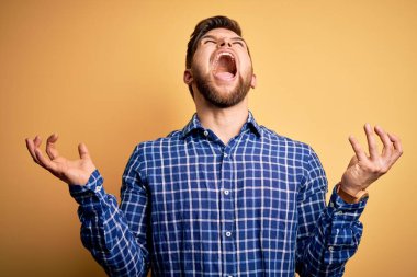 Sarışın, sakallı ve mavi gözlü genç işadamı sarı arka planda gömlek giyiyor deli deli deli bağırıyor ve agresif bir ifade ve kollarla bağırıyor. Hayal kırıklığı konsepti.