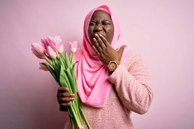 Genç Afro-Amerikan artı boy kadın elinde pembe lale buketi tutan Müslüman başörtüsü takıyor. Elle ağzını kapatmaktan sıkılmış. Huzursuz ve uykulu..