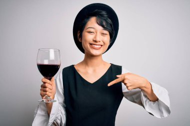 Güzel Asyalı şarap garsonu kız izole edilmiş beyaz arka planda bir bardak kırmızı şarap içerken kendini gösteren sürpriz bir yüz ifadesi takındı.