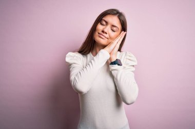 Mavi gözlü genç bir kadın pembe arka planda günlük beyaz tişört giyip uyur, yorgun düşler kurar ve elleri ile birlikte poz verir, gözleri kapalı gülümser..