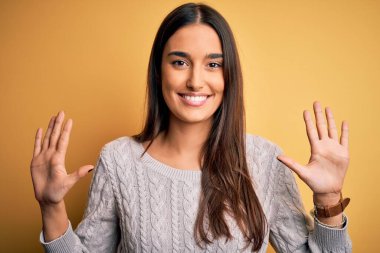 Sarı arka planda beyaz süveter giyen genç, güzel esmer kadın on numarayı gösterirken kendinden emin ve mutlu bir şekilde gülümsüyor..
