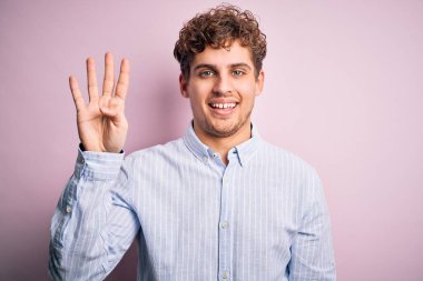 Sarışın, kıvırcık saçlı, beyaz arka planda çizgili gömlek giyen ve dört numarayı işaret eden genç, kendine güvenen ve mutlu bir adam..