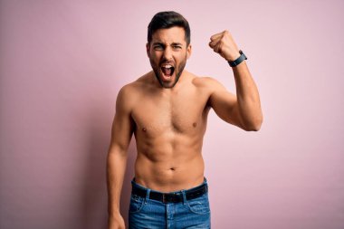 Sakalsız, genç ve güçlü bir adam pembe arka planda dikiliyor kızgın ve kızgın yumruğunu kaldırıyor ve öfkeyle bağırıyor. Öfke ve agresif kavram.