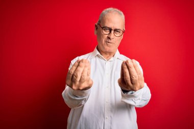 Orta yaşlı yakışıklı, beyaz gömlekli, kırmızı arka planda gözlüklü adam. Elleriyle para hareketi yapıyor. Maaş ödemesi istiyor.