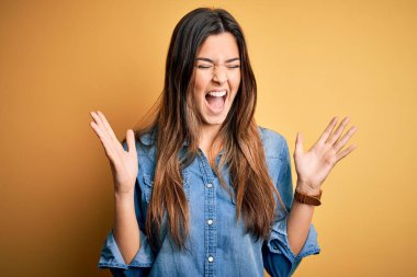 İzole edilmiş sarı arka plan üzerinde dikilmiş kollarını kaldırmış, gözlerini kapatmış heyecanlı çığlıklar atarak başarı için deli ve çılgın bir kutlama yapan genç ve güzel bir kız. Kazanan konsept