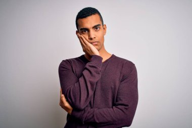 Beyaz arka plan üzerine günlük süveter giyen genç ve yakışıklı Afro-Amerikalı adam çapraz kollu depresyon sorunlarından sıkılmış ve yorgun görünüyor..