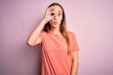Genç, güzel bir kadın, pembe arka plan üzerinde sıradan bir tişört giyip şaşkın şaşkın davranışlar sergiliyor. İnançsız ifade.
