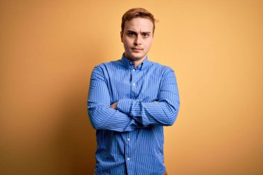 İzole edilmiş sarı arka plan şüphecisi ve gergin, kollarını çapraz yapmış, tasvip etmeyen bir yüz ifadesi takınan, sıradan çizgili tişört giyen genç, yakışıklı bir kızıl. Negatif kişi.