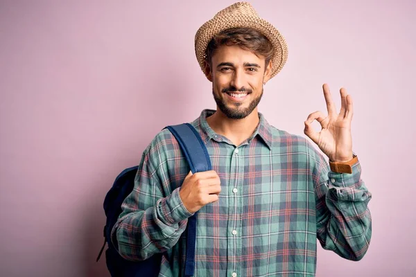 若い観光客の男で休暇を着てバックパックと夏の帽子ピンクの背景の上に指でOkサインをして 優れたシンボル — ストック写真