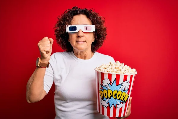 Middle age curly hair woman watching movie using 3d glasses eating popcorns annoyed and frustrated shouting with anger, crazy and yelling with raised hand, anger concept