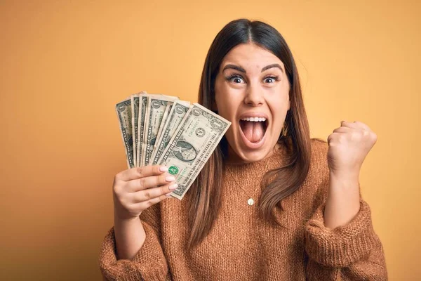 Young Beautiful Woman Holding Dollars Standing Isolated Orange Background Screaming — 스톡 사진