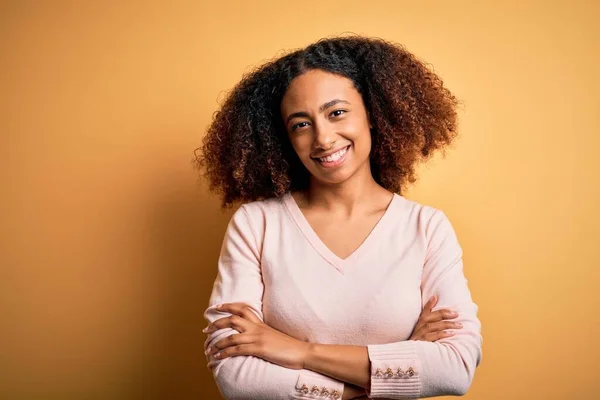 黄色の背景の幸せな顔の上にカジュアルなセーターを着てアフロの髪を持つ若いアフリカ系アメリカ人の女性は カメラを見て交差腕で笑顔 正の人 — ストック写真