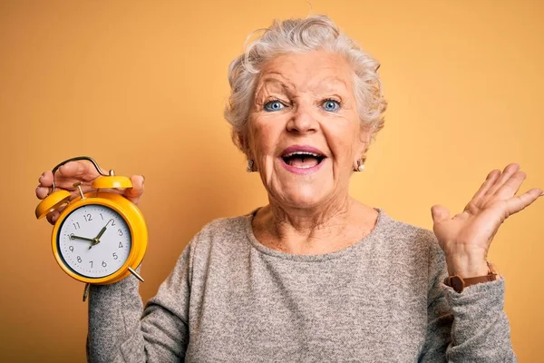 Senior Beautiful Woman Holding Alarm Clock Standing Isolated Yellow Background — Stock Photo, Image
