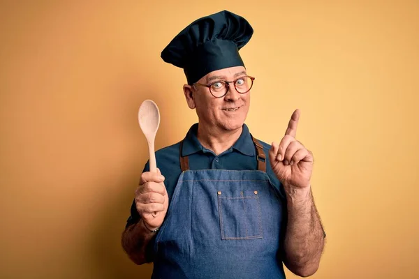 앞치마를 숟가락을 중년의 요리사 얼굴로 손가락을 가리키는 아이디어나 질문에 — 스톡 사진