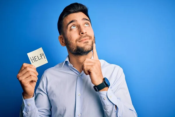 青の背景に深刻な顔を持つ紙を保持するために助けを求めている若い過労したビジネスマン質問について考えて 非常に混乱したアイデア — ストック写真