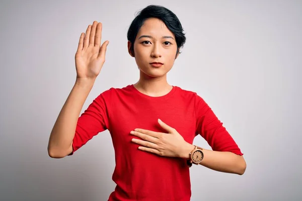 年轻美丽的亚洲女孩穿着宽松的红色T恤 站在孤立的白色背景之上 双手放在胸前 张开手掌 发誓效忠 — 图库照片