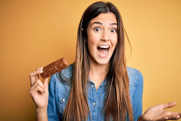 Young Beautiful Girl Holding Healthy Protein Bar Standing Isolated Yellow — Stock Photo, Image