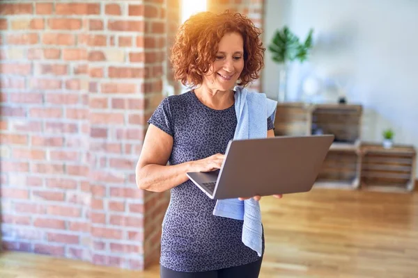 Middle age beautiful sportwoman smiling happy and confident. Standing with smile on face using laptop before doing exercise at gym