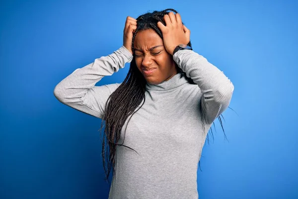 Young african american woman standing wearing casual turtleneck over blue isolated background suffering from headache desperate and stressed because pain and migraine. Hands on head.
