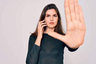 Akıllı telefondan konuşan genç güzel bir kadın izole edilmiş bir arka plan, açık elle dur işareti, ciddi ve kendinden emin bir ifade ve savunma hareketi yapıyor.