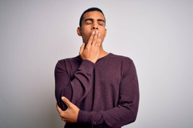 Beyaz arka plan üzerine gündelik süveter giyen genç ve yakışıklı Afro-Amerikalı adam ağzıyla esnemekten sıkılmış. Huzursuz ve uykulu..